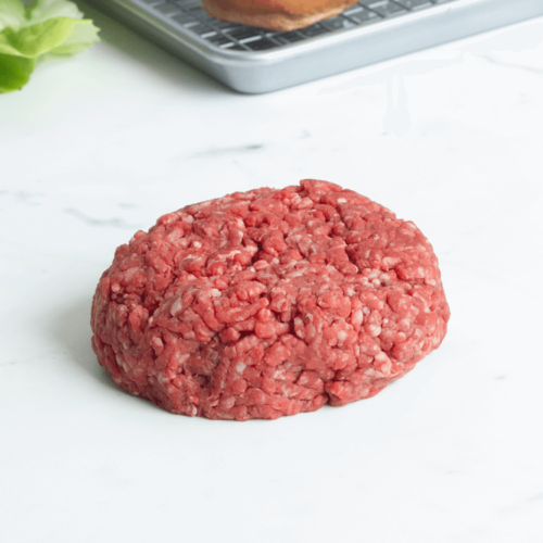Raw dry aged burger patty on a marble countertop