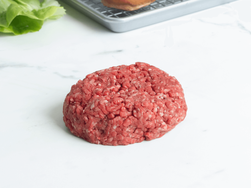 Raw dry aged burger patty on a marble countertop